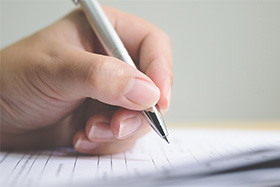 hand holding pen that is writing on paper